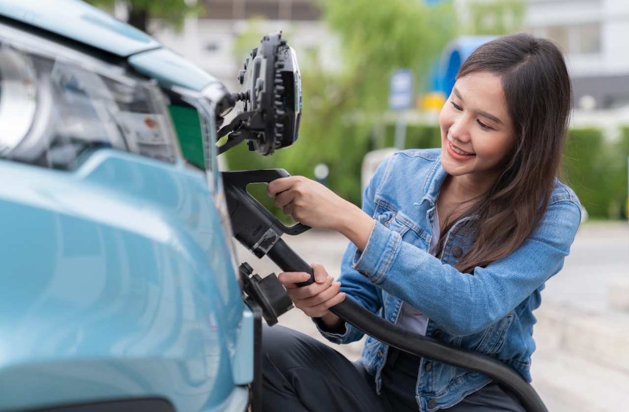 Asia woman holding AC type 2 power cable plug connect to EV car at charging station. Car driven by electric motor engine for clean environment. Rechargeable vehicle concept. Ecology green technology